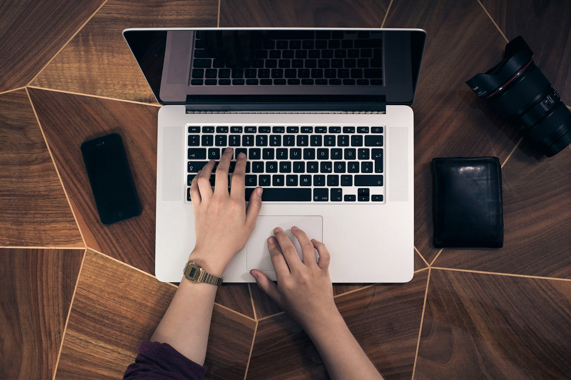 Picture of hands typing at a laptop which is placed on a wooden table.