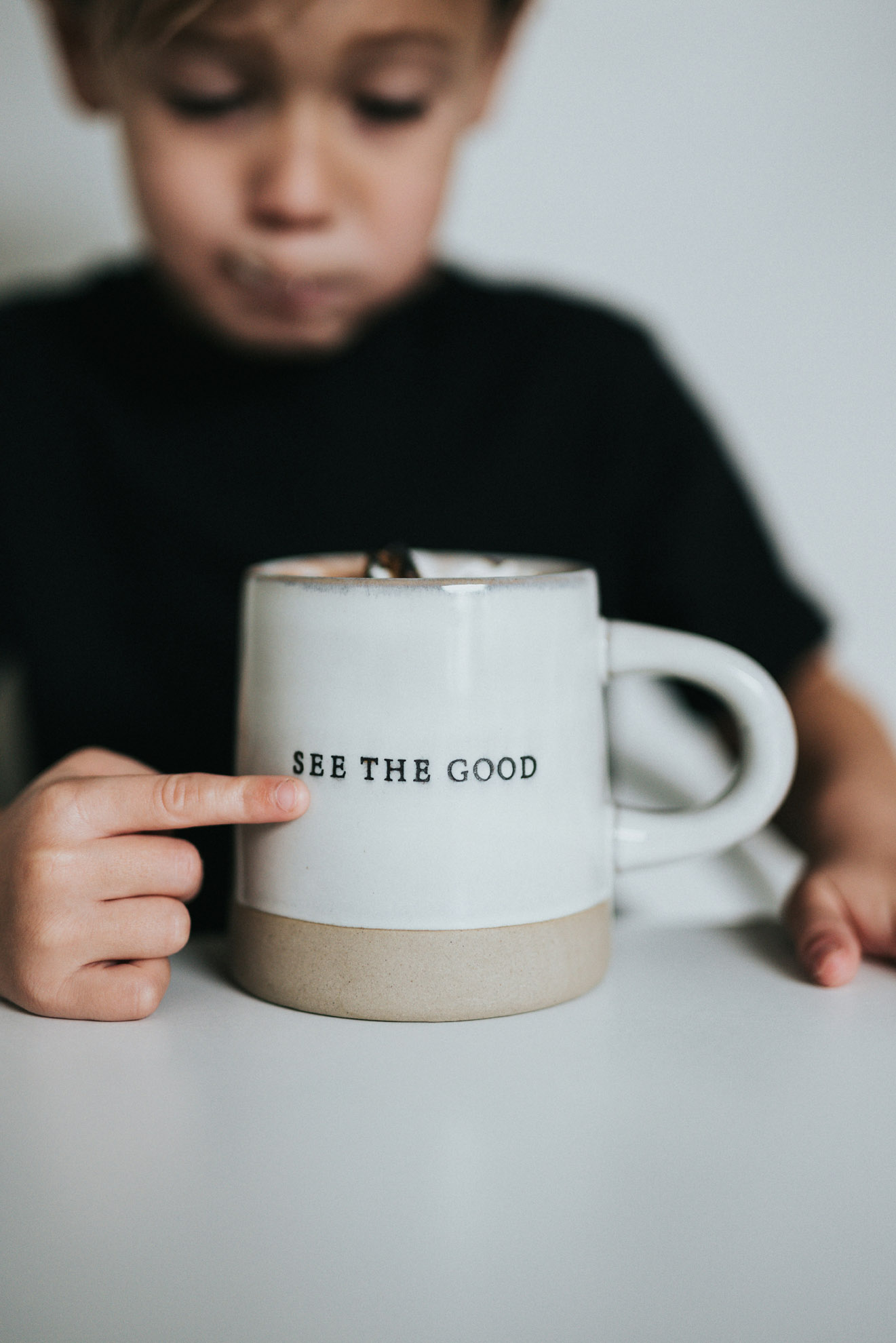 Picture of a boy pointing a finger at a cup. The text on the cup reads See The Good